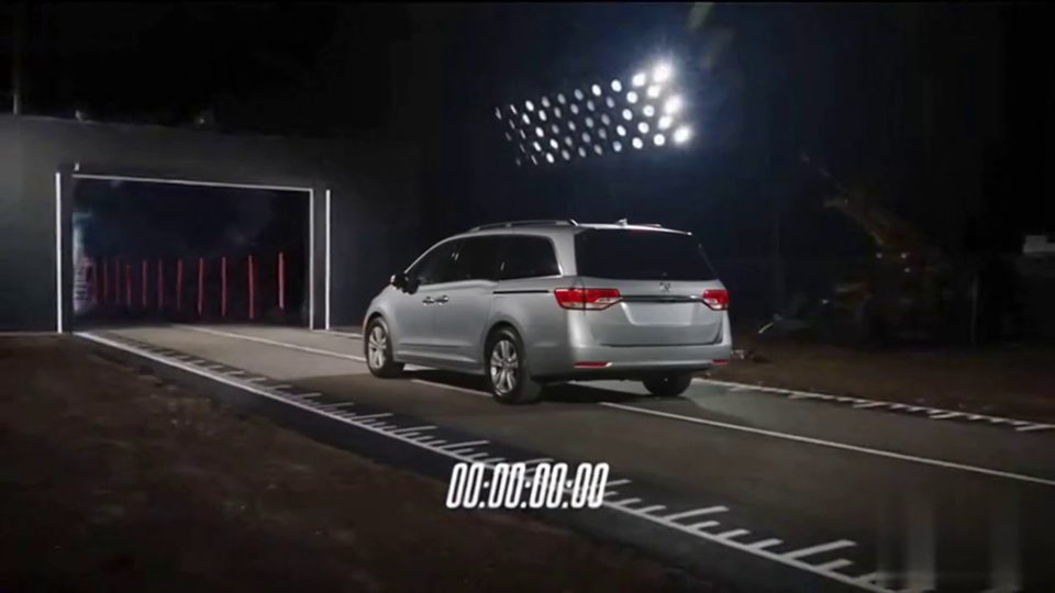 Frame from the Tesla Roadster 0-60 AI video scene: a silver minivan, seen from behind, on a floodlit test strip at night with a timer reading zero